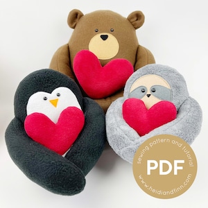 May include: Sewing pattern and tutorial PDF for making plush animal toys. The pattern includes a brown bear, a penguin, and a sloth, each holding a red heart. The PDF is available for download from www.heidianfinn.com.