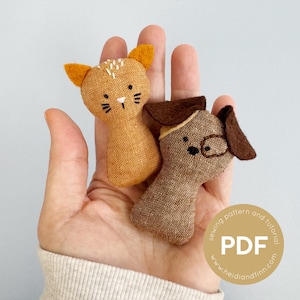 May include: Two handmade fabric animal toys: a cat and a dog. The cat is orange with yellow ears and white details. The dog is brown with dark brown ears. The toys are small and appear to be made from textured fabric.