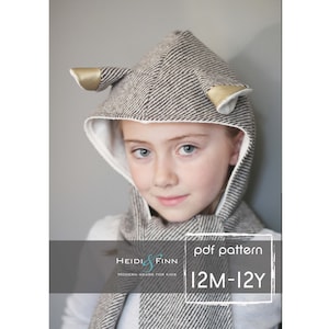 May include: A brown and white hooded scarf with gold ears. The scarf is made of a soft, textured fabric. The hood has a white lining. The scarf is for children and has the text "Heidi & Finn Modern Wear for Kids pdf pattern 12M-12Y" on it.