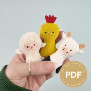 May include: Three handmade fabric finger puppets: a white lamb, a yellow chick with a red comb, and a black and white cow. The puppets are held in a hand against a light blue background. A circular graphic with the text "PDF" is in the lower right corner.