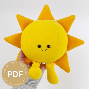 Pode incluir: Um sol de pelúcia amarelo com um rosto sorridente, raios laranja e pequenas pernas amarelas. O sol está sendo segurado por uma pessoa. Um gráfico circular com o texto "PDF" está no canto inferior esquerdo.