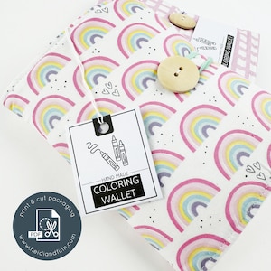May include: A handmade coloring wallet featuring a rainbow design in pink, yellow, and blue. The wallet is fastened with a wooden button. A tag with crayon illustrations reads "COLORING WALLET". The packaging is labeled "print & cut packaging".