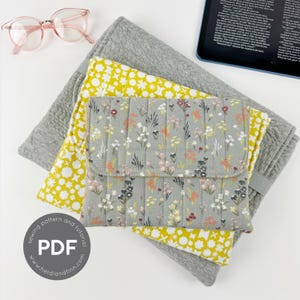 May include: Three fabric pouches with floral and geometric patterns. The pouches are stacked on top of each other. The top pouch is gray with a floral pattern, the middle pouch is yellow with a geometric pattern, and the bottom pouch is gray with a textured pattern. The text "sewing pattern and tutorial" is printed on a white circle with a black border. The text "PDF" is printed in large, bold, white letters on the circle. The text "www.heidianfinn.com" is printed in black letters below the circle.