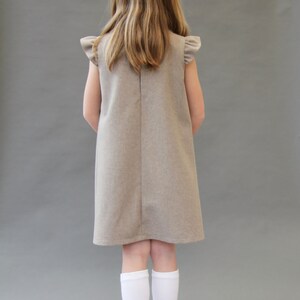 May include: A young person wearing a brown sleeveless dress with ruffled sleeves and white knee-high socks with a floral design. The socks have a pink, yellow, and green floral pattern.