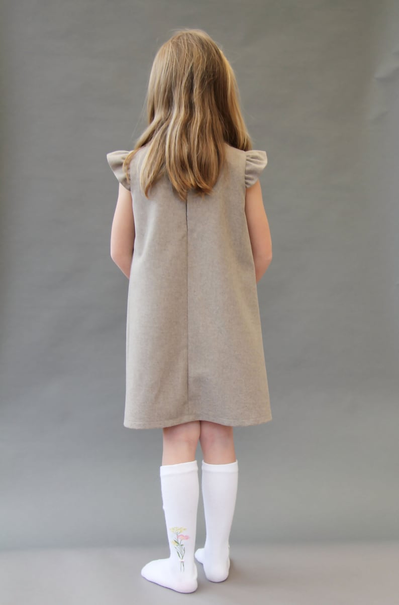 May include: A young person wearing a brown sleeveless dress with ruffled sleeves and white knee-high socks with a floral design. The socks have a pink, yellow, and green floral pattern.