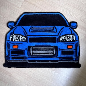 Peut inclure: Un tapis bleu en forme de voiture avec des détails noirs. Le tapis représente l'avant d'une voiture, avec des phares, une calandre et un pare-chocs. Le tapis est fait d'une matière douce et moelleuse, idéal pour un passionné de voitures.