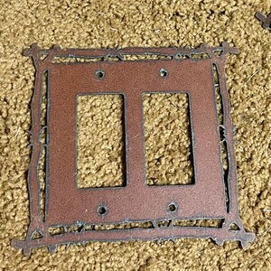 May include: A rustic brown metal double light switch cover with a decorative barbed wire design.