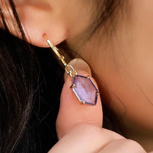 May include: Gold dangle earrings with a purple hexagonal gemstone.