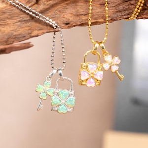 May include: Two necklaces with pendants hanging from a wooden branch. One necklace is silver with a lock and key pendant, and the other is gold with a lock and key pendant. The pendants have a floral design with opalescent stones.