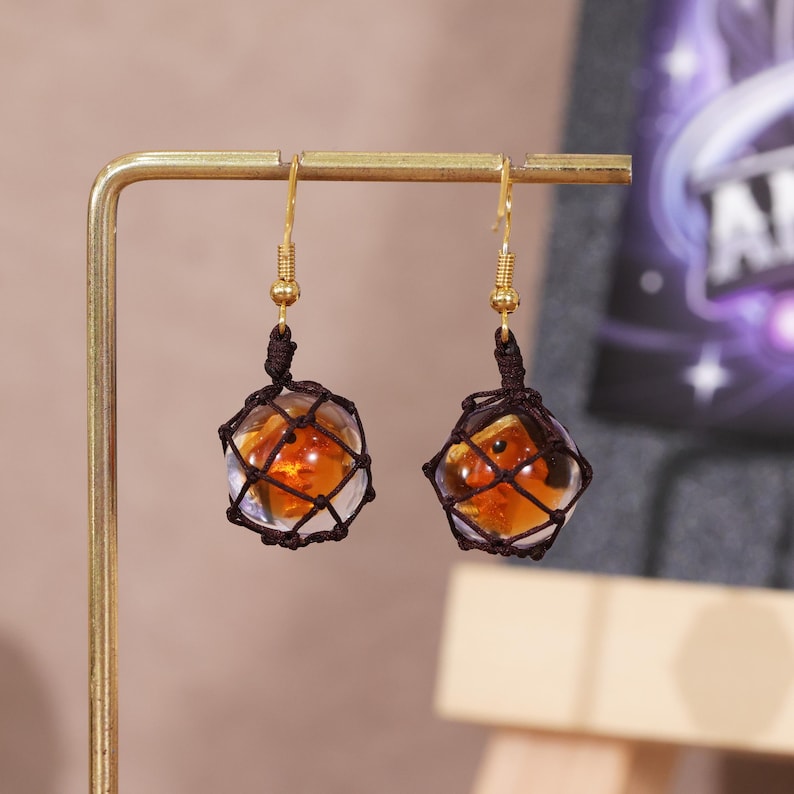 Close-up image of the handmade Splatoon-themed resin earrings, highlighting the fine detail of the fish egg texture, the reflective quality of the golden-orange resin, and the intricately woven mesh netting. The gold-plated copper hook is visible, showing the polished finish and how it complements the amber resin. This product shot emphasizes the quality and creativity of the design, ideal for Etsy shoppers searching for fandom earrings, gamer girl jewelry, or unique handmade accessories.