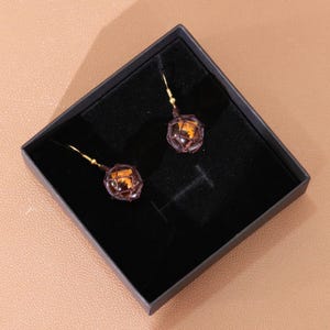 Styled image of the earrings displayed on a minimalist background, enhancing the vibrant amber color of the resin and contrasting beautifully with the dark mesh netting. The photo aims to highlight the elegance and geeky charm of these dangle earrings, perfect for Nintendo enthusiasts, Splatoon collectors, or customers searching for handmade resin jewelry with a fun twist. These earrings are suitable for daily wear or special occasions.