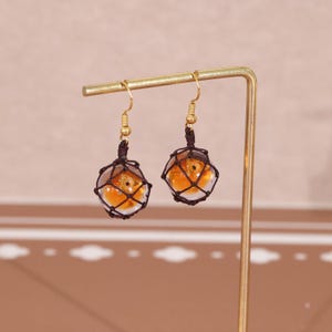 Earrings pictured against a Splatoon-themed backdrop to emphasize the video game inspiration behind the design. The golden fish egg resin charms closely resemble the in-game item from Salmon Run, making them an ideal gift for fans of the series. This visual is meant to capture the attention of Etsy users looking for handmade Splatoon merch, gamer gifts, or stylish geek jewelry with a handmade, fandom-focused design.