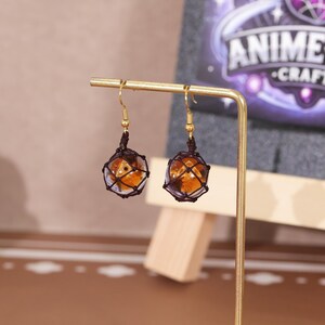 Styled image of the earrings displayed on a minimalist background, enhancing the vibrant amber color of the resin and contrasting beautifully with the dark mesh netting. The photo aims to highlight the elegance and geeky charm of these dangle earrings, perfect for Nintendo enthusiasts, Splatoon collectors, or customers searching for handmade resin jewelry with a fun twist. These earrings are suitable for daily wear or special occasions.