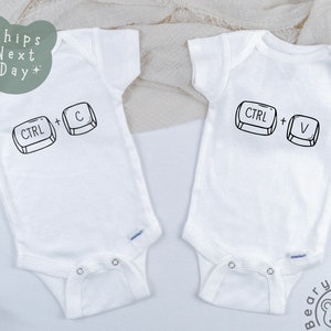 May include: Two white baby onesies with black text and images. One onesie says "CTRL + C" with a keyboard icon of the control key and the letter C. The other onesie says "CTRL + V" with a keyboard icon of the control key and the letter V.