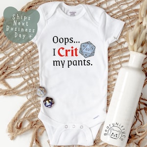 May include: White baby onesie with the text "Oops... I Crit my pants." and a blue and gray twenty-sided die graphic. The onesie is short-sleeved and has snap closures. The onesie is on a woven surface with a white vase and dried plants.