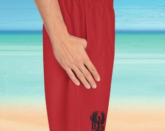 Könnte beinhalten: Rote Badeshorts mit einem schwarzen Grafikdesign am unteren rechten Bein. Die Shorts bestehen aus leichtem Material und haben einen elastischen Bund. Die Grafik scheint ein stilisierter Vogel oder Phönix zu sein.