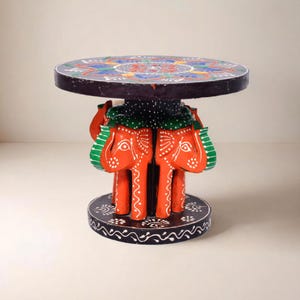 Peut inclure: Une table d'appoint artisanale avec un plateau rond orné d'un motif floral coloré. La table est soutenue par quatre éléphants oranges avec des détails blancs. La base est noire avec des motifs blancs. Un meuble unique.