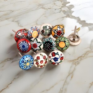 Peut inclure: Ensemble de boutons de meubles décoratifs en céramique avec divers motifs floraux. Les boutons présentent une gamme de couleurs, dont le rouge, le bleu, le jaune et le vert, avec des tiges métalliques. Les boutons sont disposés sur une surface en marbre.