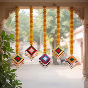 Può includere: Cinque ghirlande decorative appese. Ogni ghirlanda presenta una fila di fiori gialli e arancioni, con un ornamento a forma di diamante colorato in basso. Gli ornamenti hanno nappe e piccole campane, con accenti rossi, bianchi, blu e verdi.