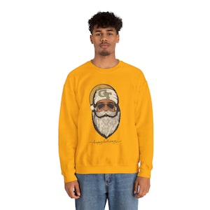 May include: Mustard yellow sweatshirt featuring a Santa Claus graphic with sunglasses, a beard, and a hat. The hat has the letters "GT" on it. The words "happy holidays" are written in cursive below the graphic.