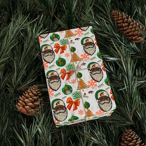 Peut inclure: Cadeau emballé avec un motif festif représentant un Père Noël, des sapins de Noël, des flocons de neige et des nœuds. Le papier d'emballage est blanc avec des accents orange, verts et marron. Attaché avec de la ficelle, le cadeau est posé sur un fond d'aiguilles de pin et de pommes de pin.