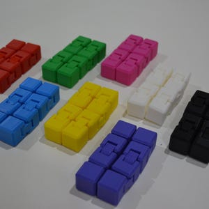 May include: A selection of colourful fidget toys in red, green, pink, white, blue, yellow, purple, and black. Each toy is made of connected cubes, designed for tactile manipulation and stress relief. The toys are arranged on a white surface.