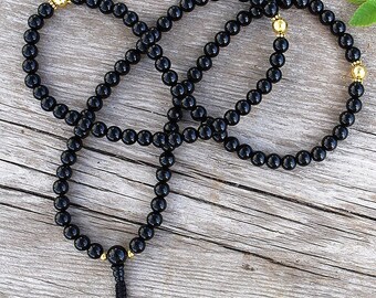 May include: Black beaded necklace with gold accents. The necklace is made of round beads and has a tassel at the end.