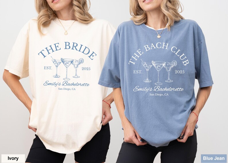 May include: Two short-sleeved t-shirts, one ivory and one blue, with matching text and graphics. The ivory shirt reads "THE BRIDE" above three cocktail glasses, and the blue shirt reads "THE BACH CLUB". Both shirts include "Emily's Bachelorette, San Diego, CA" and the year 2025.