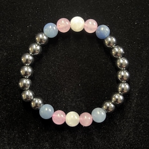 May include: A beaded bracelet featuring alternating silver-colored metallic beads and colorful gemstone beads. The gemstone beads are light blue, pink, and white. The bracelet is displayed on a black surface.
