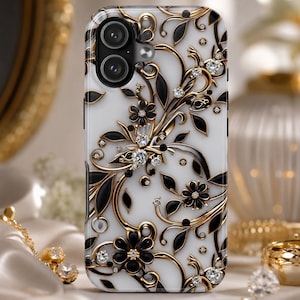 May include: A white smartphone case featuring a decorative pattern of black and gold swirling floral vines and leaves. The design is accented with small, clear, sparkling crystals embedded throughout the floral and vine motifs.