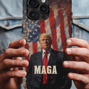 May include: A black phone case featuring a portrait of a man in a suit and red tie, set against a backdrop of the American flag. The word "MAGA" is prominently displayed in white block letters.