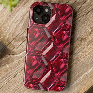 May include: A smartphone case with a vibrant, gem-like pattern in shades of red. The case features a glossy finish and a design that mimics the facets of cut gemstones. The phone's camera lenses are visible at the top.