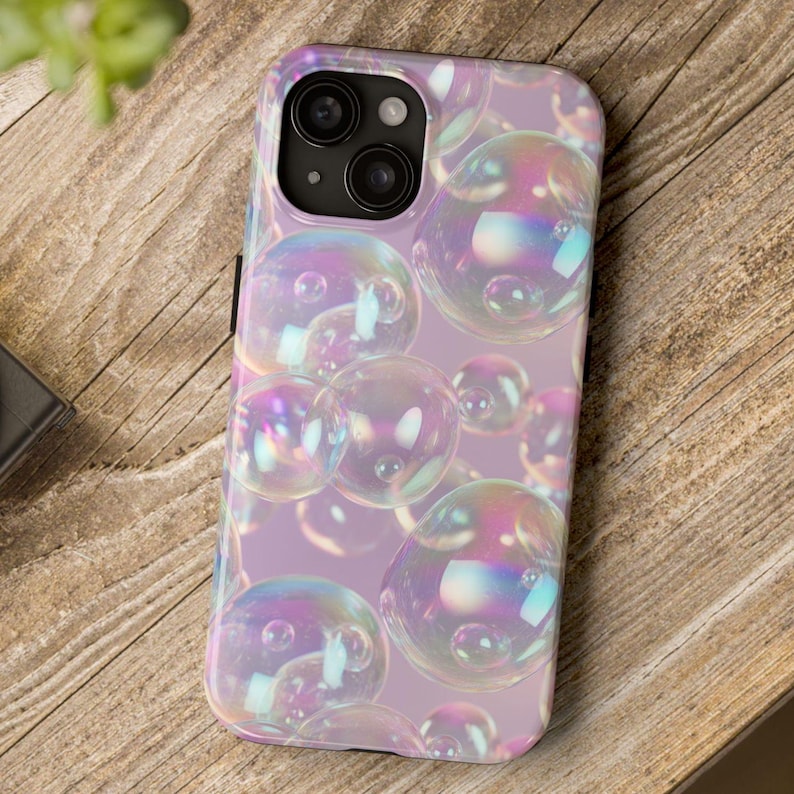 May include: iPhone 13 Pro Max case featuring a pastel purple background adorned with iridescent bubbles. The case showcases a vibrant, colorful design with a variety of bubble sizes and shapes, creating a whimsical and dreamy aesthetic.  The phone case is compatible with the iPhone 13 Pro Max model, offering full protection and showcasing a unique, eye-catching design.