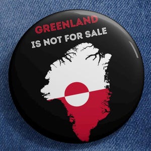 以下が含まれることがあります： 「GREENLAND IS NOT FOR SALE」の文字が赤と白で書かれた、黒い丸いボタン。ボタンには、白と赤で描かれたグリーンランドの地図があり、中央に白い円があります。