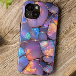 以下が含まれることがあります： 紫、青、オレンジの宝石のモザイクを特徴とする、カラフルで虹色のデザインの携帯電話ケース。ケースには、携帯電話のカメラ用の切り抜きがあります。