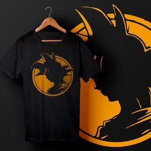 以下が含まれることがあります： 金色のシルエットが描かれた黒いTシャツ。デザインは、キャラクターの頭と肩の横顔です。画像の右側には、キャラクターの大きな金色のシルエットがあります。
