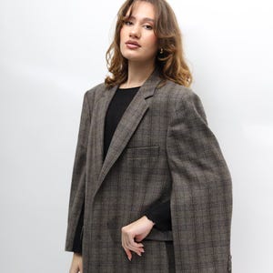 May include: A brown checked blazer with a classic design. The blazer features a notched lapel, a chest pocket, and buttoned cuffs. The model is wearing a black top. A stylish outerwear option.