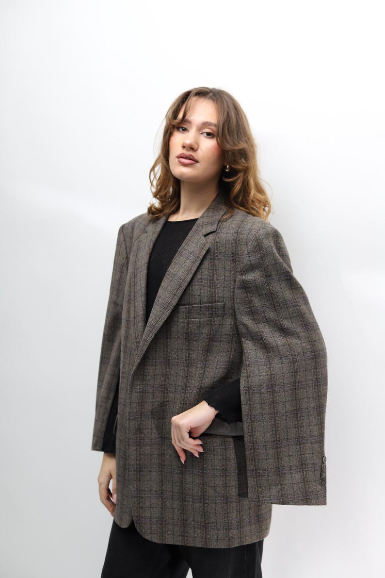 May include: A brown checked blazer with a classic design. The blazer features a notched lapel, a chest pocket, and buttoned cuffs. The model is wearing a black top. A stylish outerwear option.