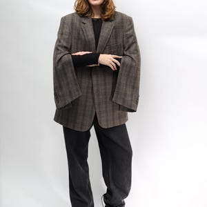 May include: A brown plaid blazer, black long-sleeve top, and black jeans. The blazer features a classic design with a notched lapel and buttoned cuffs. The jeans are dark wash, and the outfit is completed with black heeled boots.