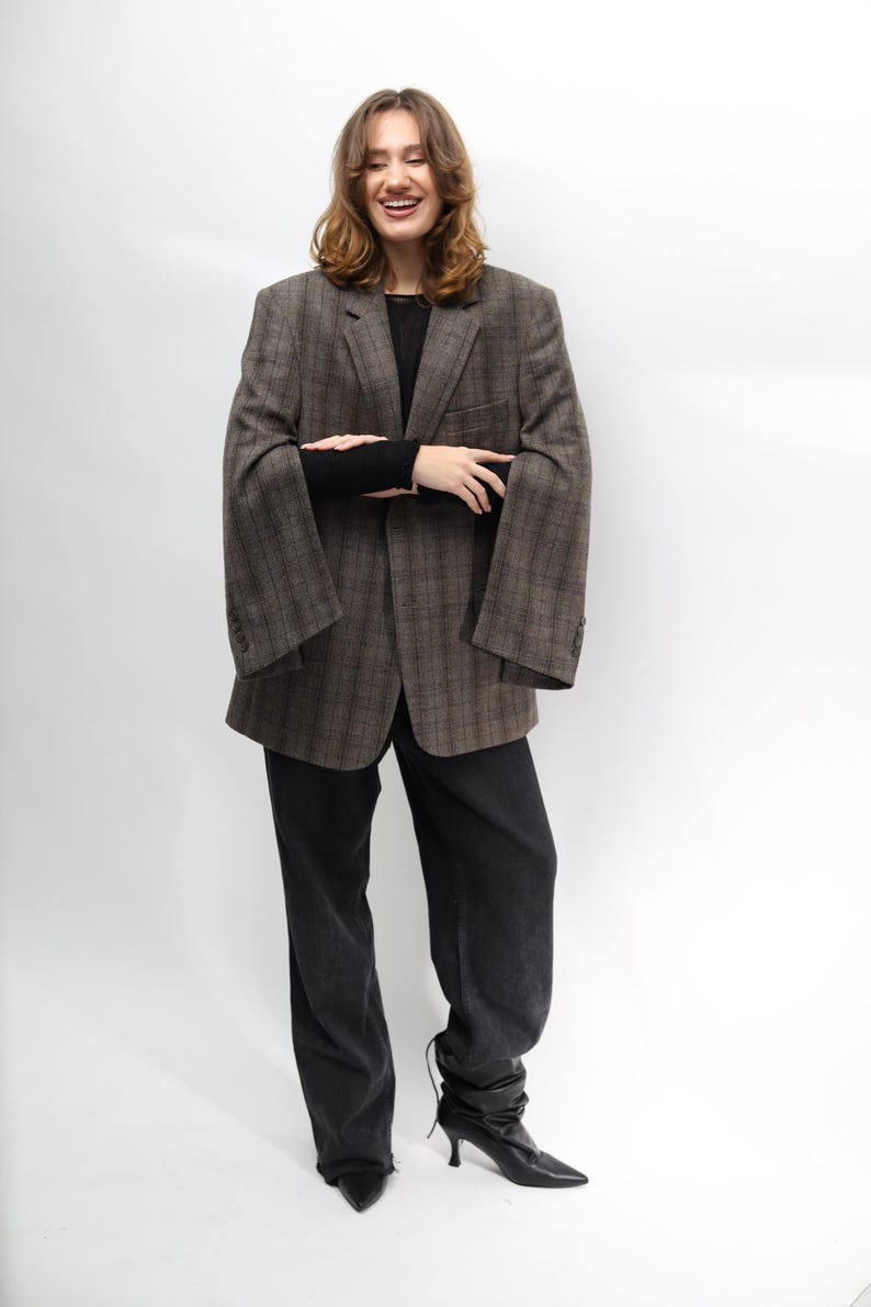 May include: A brown plaid blazer, black long-sleeve top, and black jeans. The blazer features a classic design with a notched lapel and buttoned cuffs. The jeans are dark wash, and the outfit is completed with black heeled boots.