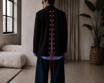 May include: Black blazer featuring red lacing detail down the back, worn over a blue shirt and paired with wide-leg denim jeans. The outfit has a minimalist, modern aesthetic.