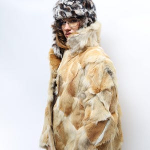 May include: A vintage fur coat and matching hat. The coat has a patchwork design in shades of tan, brown, and cream. The hat has a spotted pattern in black, white, and brown. The coat has a high collar.