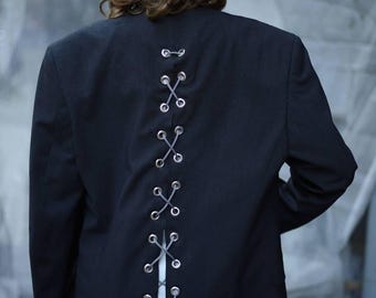 May include: A black blazer with a distinctive back detail. Silver eyelets are laced together with a grey cord, forming an X pattern down the back. This blazer combines a classic cut with a contemporary design.