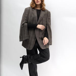 May include: A brown plaid blazer, black long-sleeve top, and black jeans. The blazer features a classic pattern and a relaxed fit. The model is wearing black heeled boots. The outfit is set against a white background.