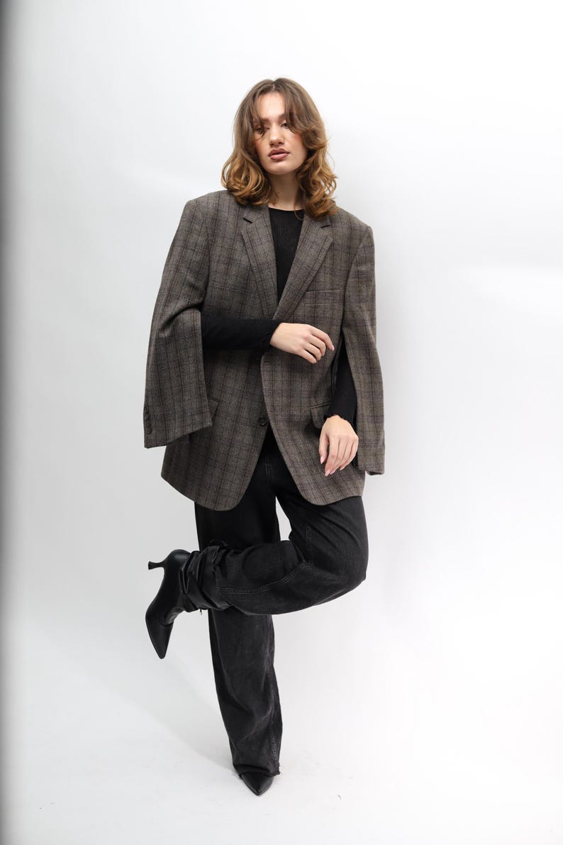 May include: A brown plaid blazer, black long-sleeve top, and black jeans. The blazer features a classic pattern and a relaxed fit. The model is wearing black heeled boots. The outfit is set against a white background.