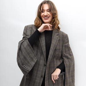 May include: A brown plaid blazer with a classic design. The blazer features a notched lapel, a two-button closure, and a tailored fit. The sleeves are long and the fabric has a subtle texture. The blazer is worn over a black top.