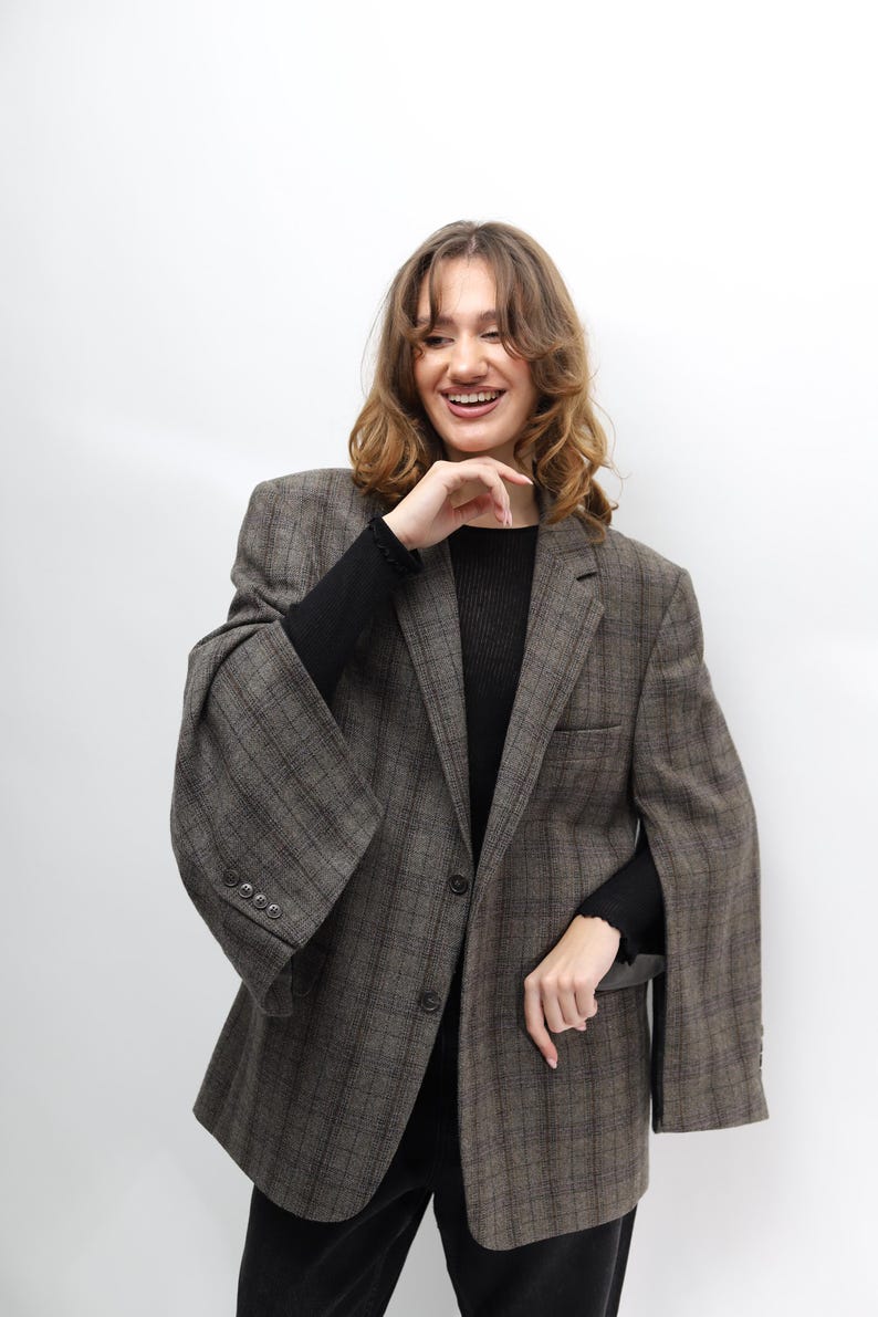 May include: A brown plaid blazer with a classic design. The blazer features a notched lapel, a two-button closure, and a tailored fit. The sleeves are long and the fabric has a subtle texture. The blazer is worn over a black top.