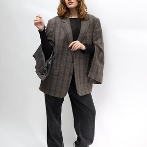 May include: A brown plaid blazer, black top, and dark wash jeans. The blazer features a classic check pattern and a relaxed fit. The jeans are a straight-leg style. The outfit is completed with black heeled boots.