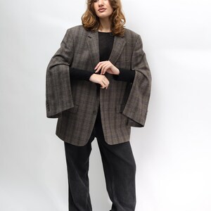 May include: A brown plaid blazer with wide sleeves, worn with black trousers and boots. The blazer features a classic check pattern and a relaxed fit. The outfit is completed with a black long-sleeve top.