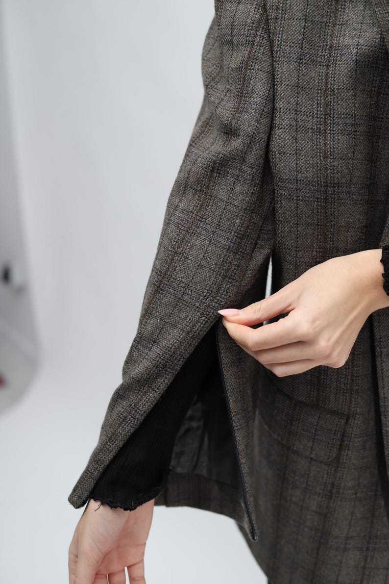 May include: A brown plaid blazer with a black lining. The blazer features a classic design with a notched lapel and a two-button closure. The fabric has a subtle texture and a muted colour palette.